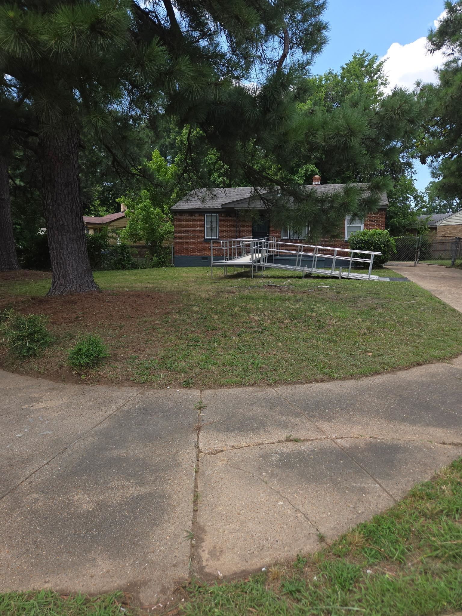 1510 Gausco Road Memphis, TN 38106 - Photo 9 of 10 Brick facade home featuring a wheelchair ramp entry, mature trees, and a sloped front lawn
