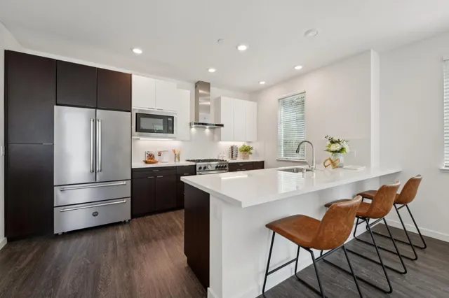 a kitchen with a refrigerator a microwave oven a sink and a dining table with wooden floor