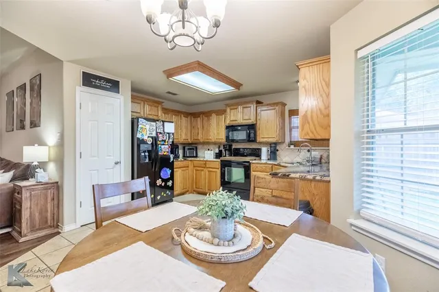 a dining room with furniture a kitchen a chandelier a wooden floor and a large window