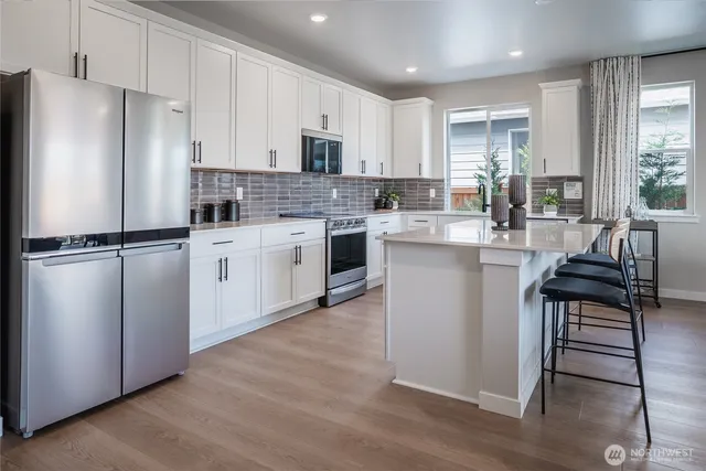 a kitchen with stainless steel appliances granite countertop a refrigerator a stove a sink and white cabinets with wooden floor