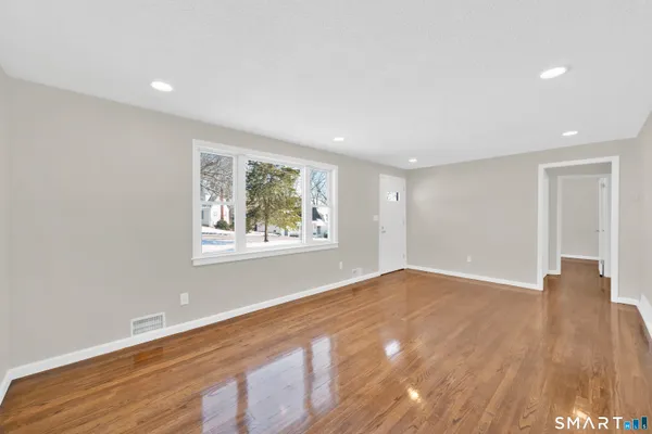 a view of an empty room with wooden floor and a window