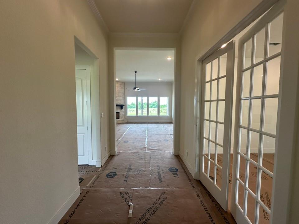 205 Cobb Road Leonard, TX 75452 - Photo 4 of 28 Hallway with protective floor covering, featuring a view into a living area with a stone-clad fireplace, a ceiling fan, and multiple windows