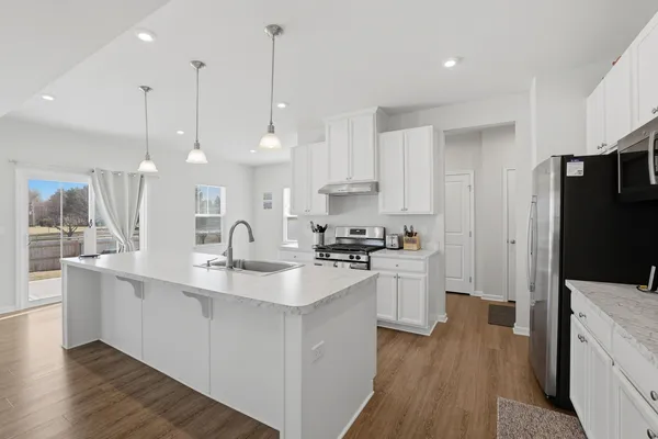 a kitchen with stainless steel appliances a sink a stove a refrigerator a center island and wooden floor