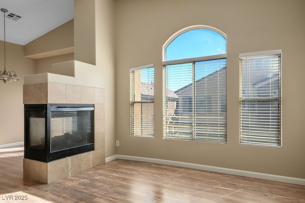 6610 Tumbleweed Ridge Lane, Unit 101 Henderson, NV 89011 - Photo 11 of 24 Unfurnished living room featuring wood finished floors, a tile fireplace, a chandelier, and high vaulted ceiling
