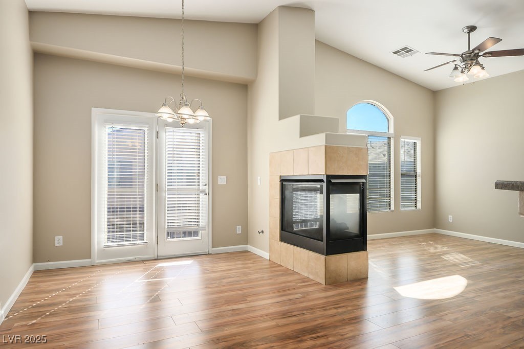 6610 Tumbleweed Ridge Lane, Unit 101 Henderson, NV 89011 - Photo 4 of 24 Unfurnished living room featuring a tile fireplace, wood finished floors, ceiling fan, a chandelier, and high vaulted ceiling