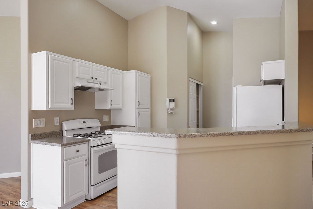 6610 Tumbleweed Ridge Lane, Unit 101 Henderson, NV 89011 - Photo 8 of 24 Kitchen featuring white appliances, under cabinet range hood, a towering ceiling, light wood-style flooring, and white cabinetry