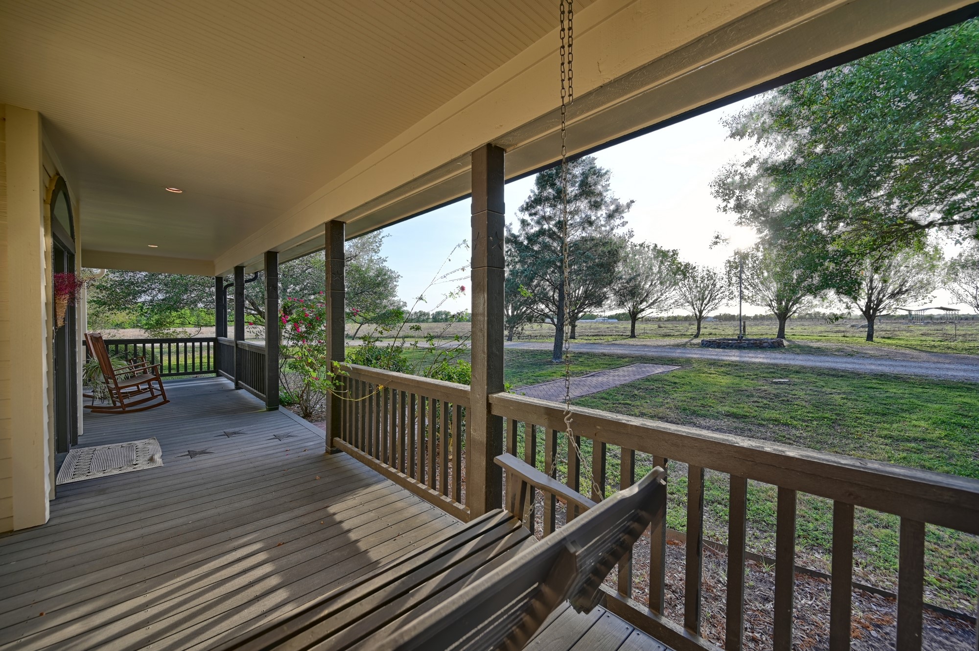 5255 Ganske Road Burton, TX 77835 - Photo 5 of 46 Covered front porch with a swing and rocking chair, overlooking a spacious yard with a tree-lined path, perfect for relaxing and enjoying the serene outdoor view.