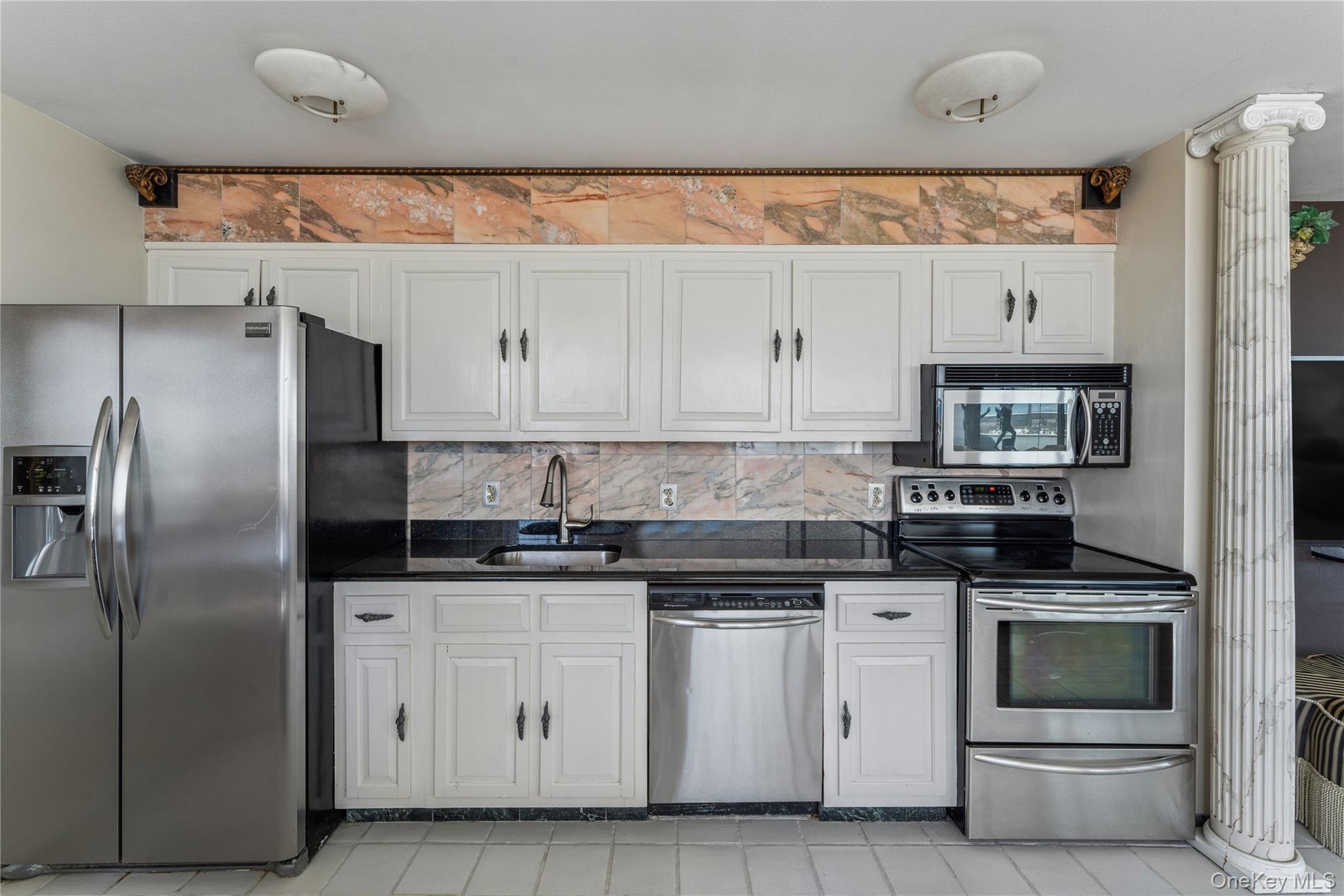 253 Dune Road, Unit 48 Westhampton Beach, NY 11978 - Photo 8 of 28 a kitchen with white cabinets and stainless steel appliances