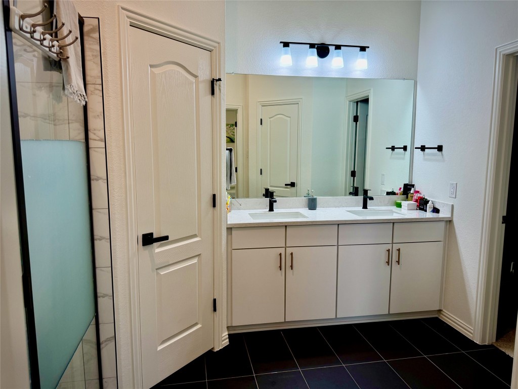 1209 Cole Ests Drive Georgetown, TX 78628 - Photo 13 of 33 Bathroom with double vanity, dark tile patterned flooring, and a shower with shower door