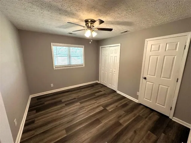 a view of an empty room with wooden floor and a ceiling fan