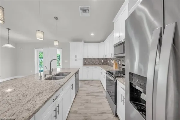 a view of kitchen with stainless steel appliances granite countertop a stove a sink a refrigerator and white cabinets with wooden floor
