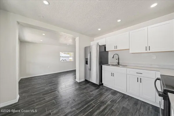 a kitchen with granite countertop a refrigerator and white cabinets