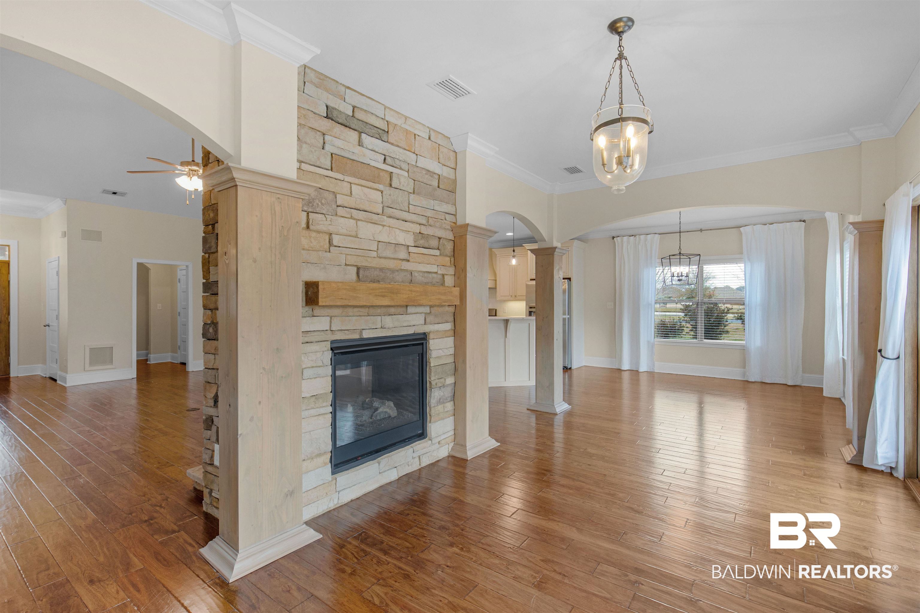 25092 Fairfax Road Daphne, AL 36526 - Photo 8 of 29 Unfurnished living room with crown molding, a fireplace, wood-type flooring, ceiling fan with notable chandelier, and ornate columns