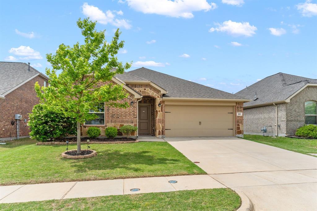 300 Copper Switch Drive Anna, TX 75409 - Photo 3 of 26 The property features a brick and stone facade, a well-maintained lawn, and a paved driveway leading to an attached garage