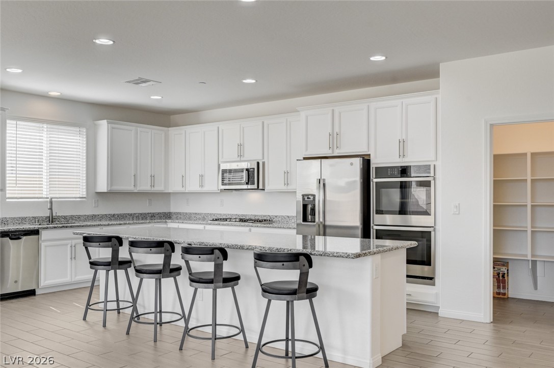 756 Cadence View Way Henderson, NV 89011 - Photo 7 of 45 Kitchen with wood finish floors, a breakfast bar area, white cabinetry, stainless steel appliances, and recessed lighting