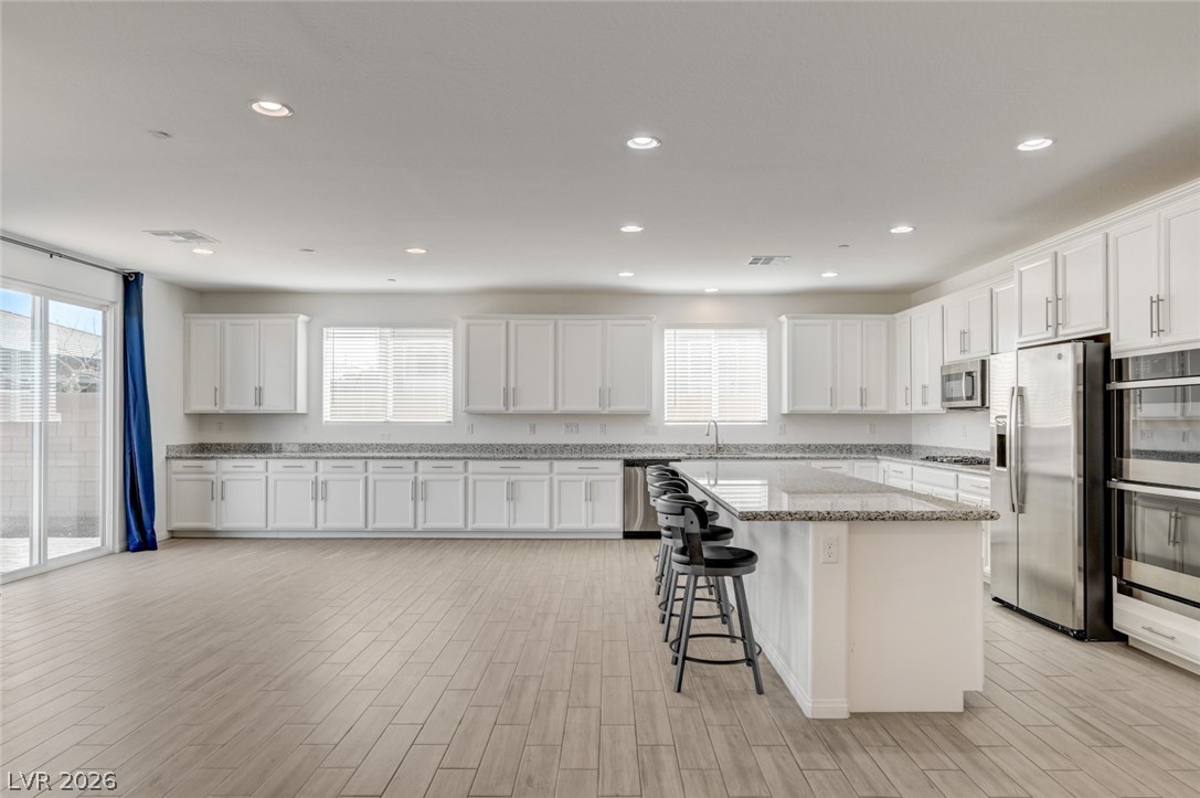 756 Cadence View Way Henderson, NV 89011 - Photo 8 of 45 Kitchen featuring white cabinetry, a kitchen bar, stainless steel appliances, wood finish floors, and recessed lighting