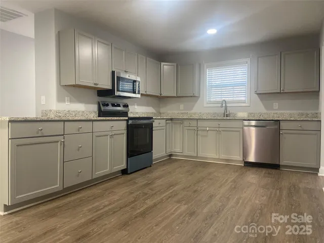 a kitchen with stainless steel appliances granite countertop a stove top oven a sink dishwasher and white cabinets with wooden floor