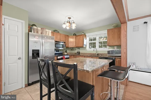 a kitchen with stainless steel appliances granite countertop a stove top oven a refrigerator a sink and a dining table with white cabinets