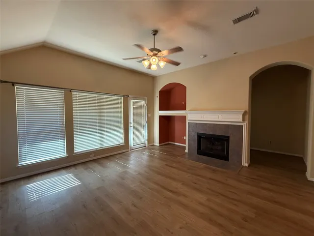 a view of an empty room with wooden floor fireplace and a window