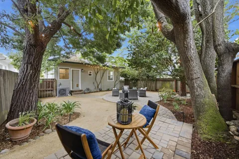 a view of a backyard with table and chairs potted plants and large tree