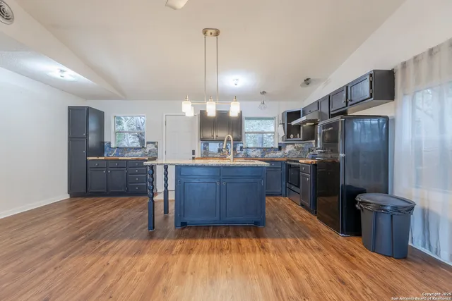 a kitchen with stainless steel appliances kitchen island granite countertop a refrigerator a sink dishwasher a stove and a wooden floors