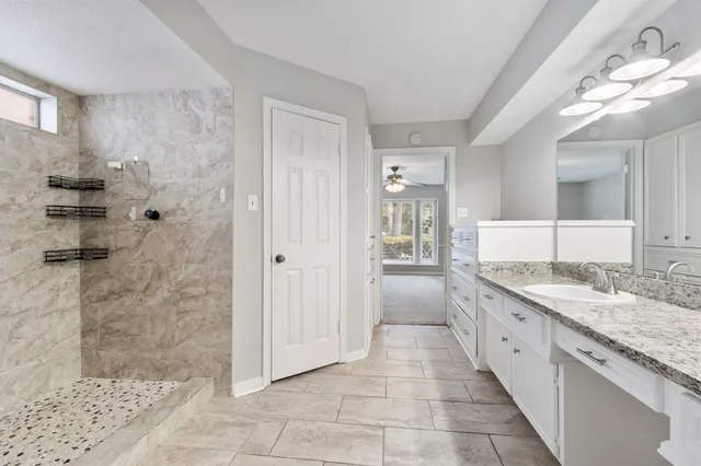 a large white bathroom with a granite countertop sink a mirror and a shower
