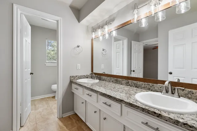 a bathroom with a granite countertop double vanity sink a mirror and a toilet