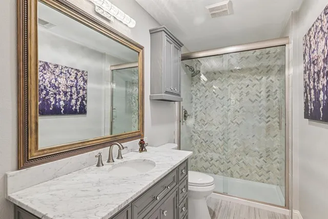 a bathroom with a granite countertop sink a mirror a toilet and a shower