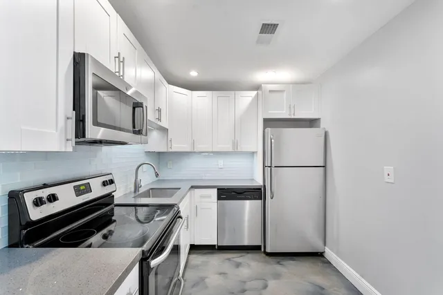a kitchen that has a refrigerator a stove and white cabinets