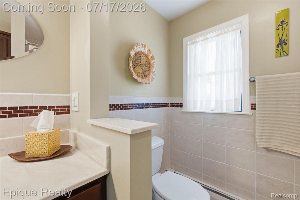 555 East Square Lake Road Troy, MI 48085 - Photo 30 of 48 Bathroom featuring a window with privacy curtain, light-toned wall tiles with a decorative accent band, and a vanity with a light-colored countertop