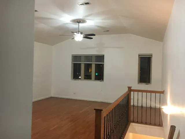 a view of an empty room with wooden floor and a ceiling fan