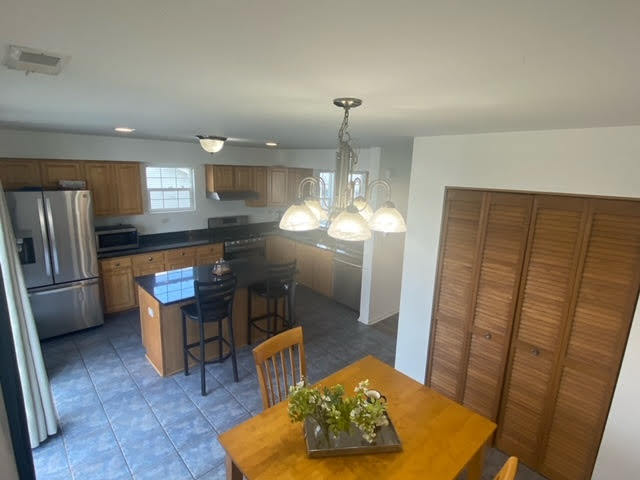 1365 Fox Hound Trail Beecher, IL 60401 - Photo 6 of 22 a kitchen with stainless steel appliances granite countertop a refrigerator a sink a dining table and chairs with wooden floor