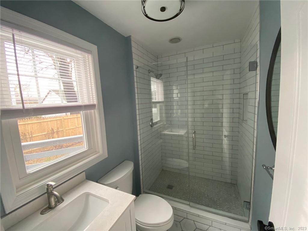 218 Ruane Street Fairfield, CT 06824 - Photo 16 of 26 a bathroom with a granite countertop toilet a sink a mirror and shower