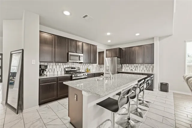 a kitchen with stainless steel appliances granite countertop a refrigerator a stove a sink a dining table and chairs