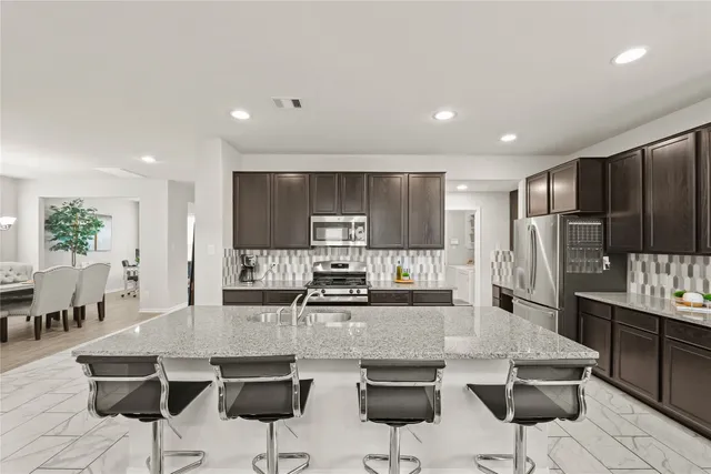 a kitchen with stainless steel appliances kitchen island granite countertop a dining table chairs refrigerator and cabinets