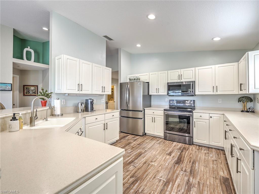 8460 Southbridge Drive, Unit 2 Estero, FL 33967 - Photo 15 of 42 a kitchen with a refrigerator a stove top oven a sink dishwasher and white cabinets with wooden floor