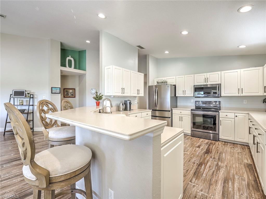 8460 Southbridge Drive, Unit 2 Estero, FL 33967 - Photo 16 of 42 a kitchen with stainless steel appliances a stove a sink a kitchen island and chairs with wooden floor
