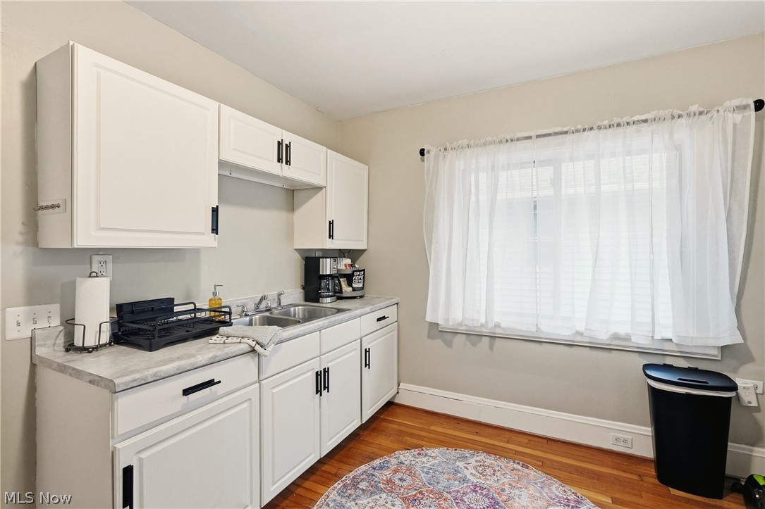 3579 Bosworth Road Cleveland, OH 44111 - Photo 17 of 39 Bright kitchen space featuring white cabinetry with black hardware, a stainless steel double sink, wood-finish flooring, and a large window with sheers