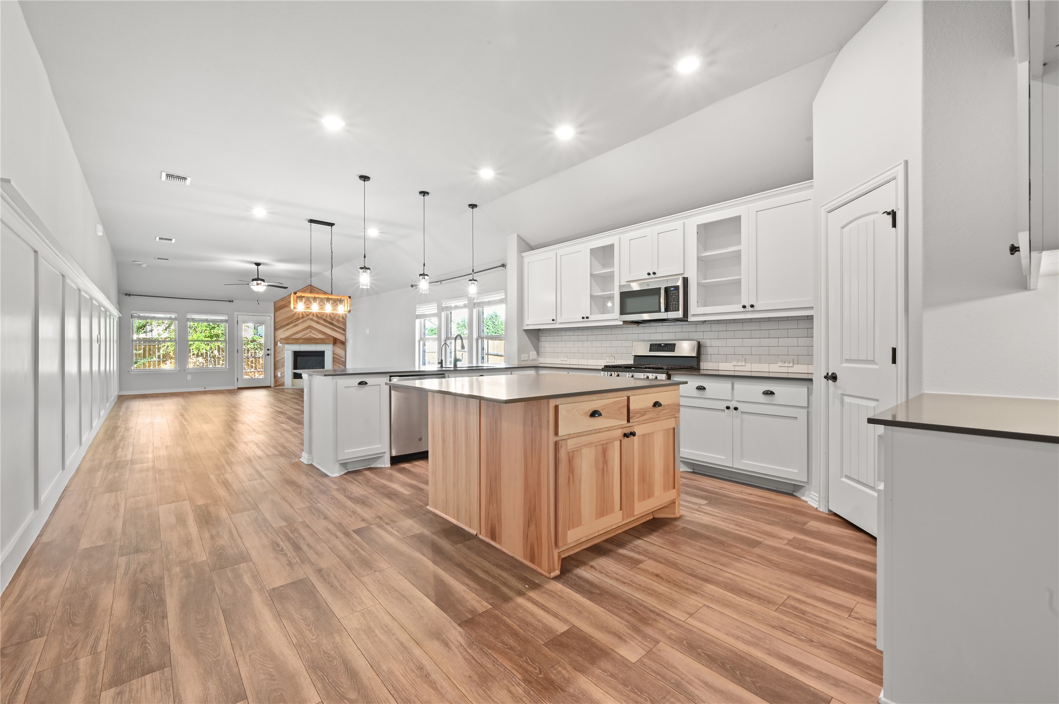 426 Cold Riv Run Kyle, TX 78640 - Photo 8 of 34 A well-lit, open-concept interior features wood flooring, a central kitchen island, and a corner fireplace, creating a spacious and inviting atmosphere.