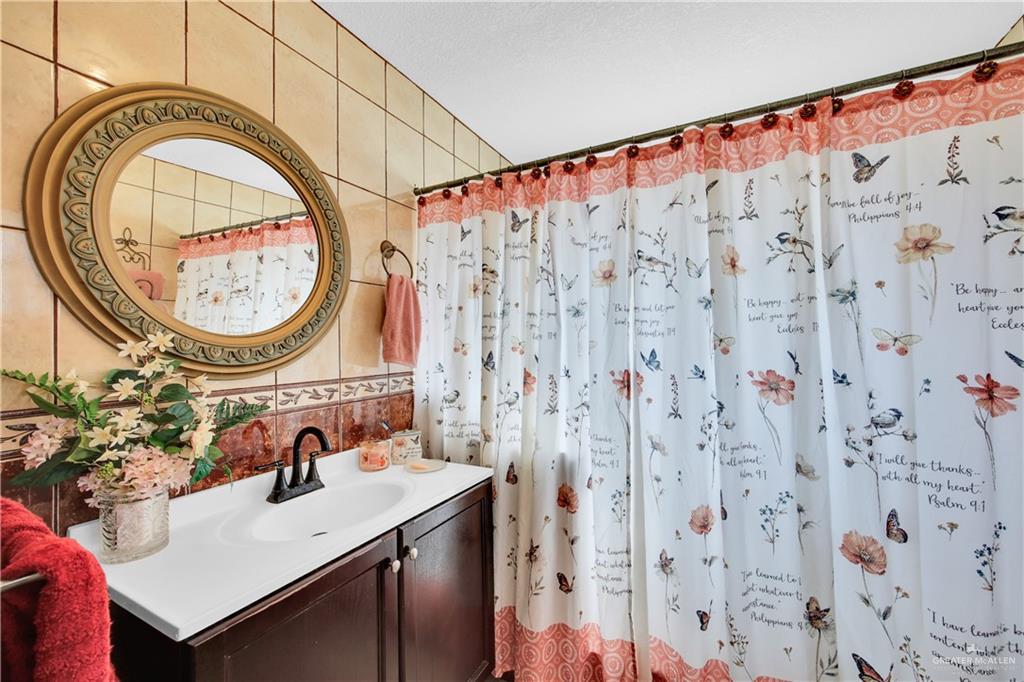 695 El Paisano Road Rio Grande City, TX 78582 - Photo 13 of 30 Bathroom with vanity, a shower with shower curtain, and tile walls