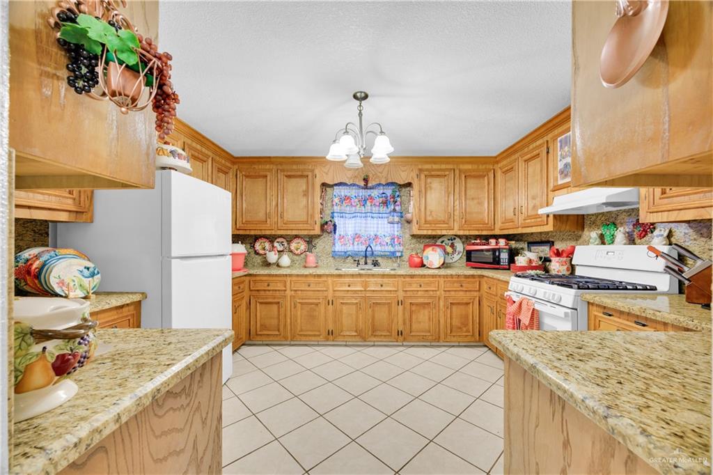 695 El Paisano Road Rio Grande City, TX 78582 - Photo 6 of 30 Kitchen featuring light stone countertops, white appliances, a chandelier, and tasteful backsplash