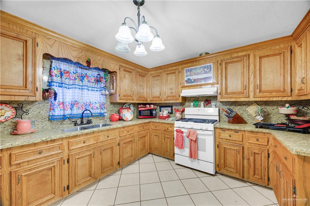 695 El Paisano Road Rio Grande City, TX 78582 - Photo 7 of 30 Kitchen with gas range gas stove, light tile patterned flooring, suspended lighting, tasteful backsplash, and light stone countertops