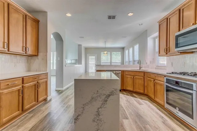 a large kitchen with stainless steel appliances granite countertop a stove a sink dishwasher and a microwave oven with wooden floor