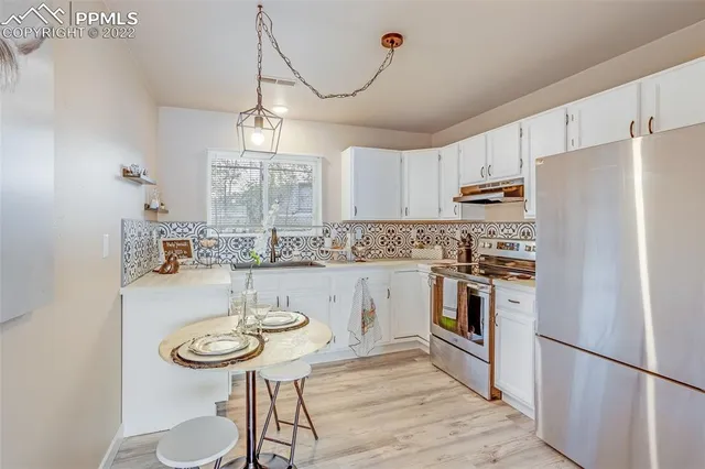 a kitchen with stainless steel appliances a sink a stove a refrigerator cabinets a dining table and chairs