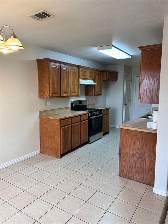 722 Rambling Court Granbury, TX 76049 - Photo 3 of 7 Kitchen with wood finish cabinetry, light countertops, stainless steel gas range, light tile patterned flooring, and a textured ceiling. New range.