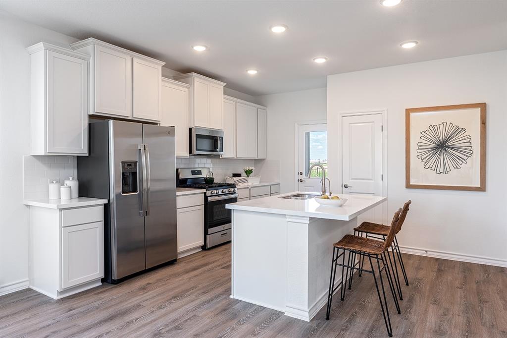 308 Stinchcomb Road Hutto, TX 78634 - Photo 6 of 14 Kitchen featuring white cabinetry, stainless steel appliances, a center island with sink, a kitchen breakfast bar, and backsplash