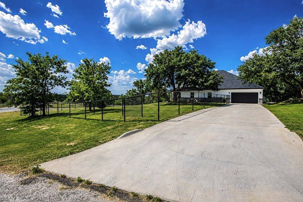 117 Rock Salt Drive Springtown, TX 76082 - Photo 34 of 38 Long concrete driveway leading to a white exterior home with a dark roof and a two-car garage
