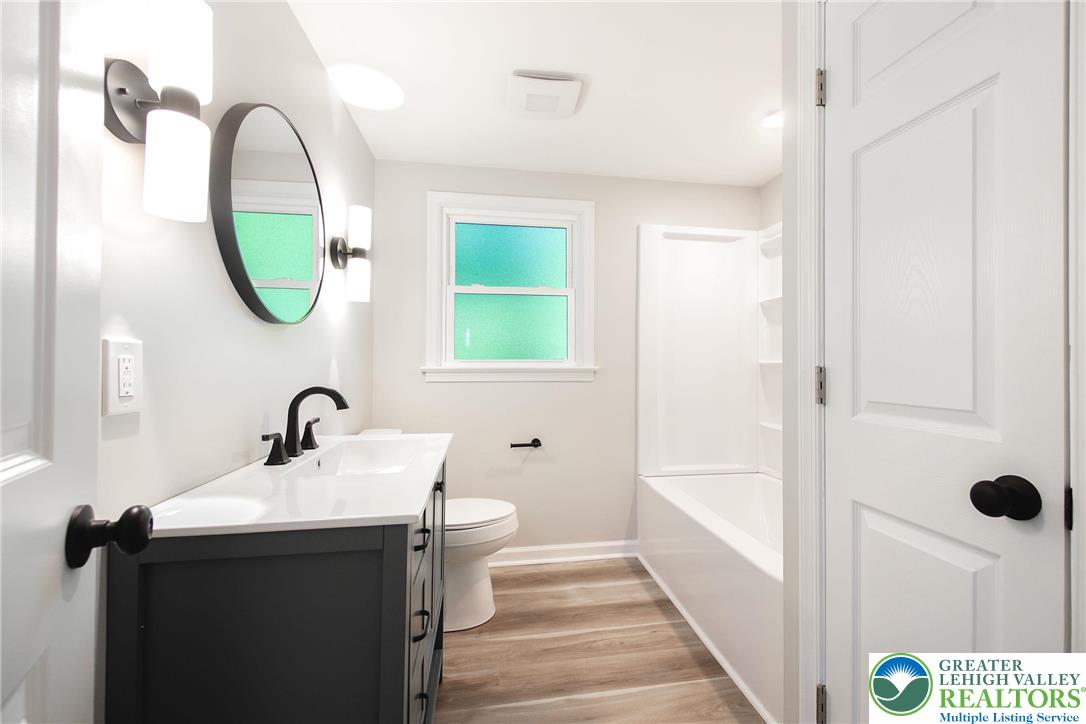 4008 State Road Coopersburg, PA 18036 - Photo 7 of 19 A well-lit bathroom features a vanity, mirror, toilet, and a combination tub-shower with modern fixtures.