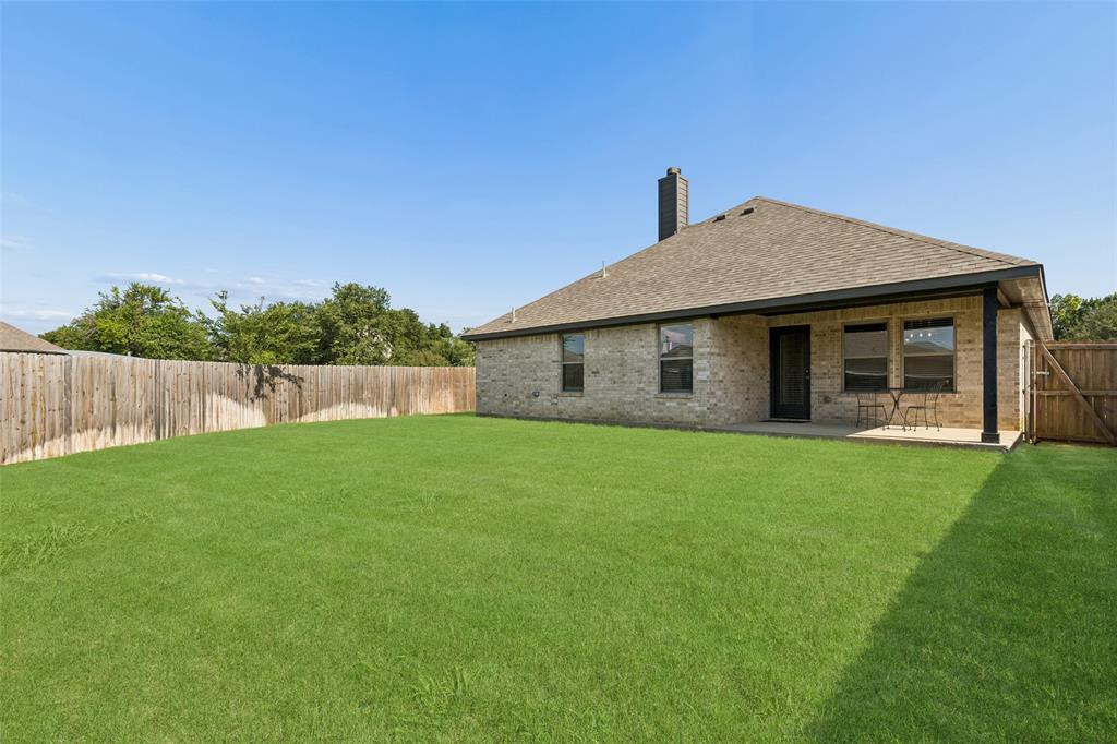 108 Maverick Lane Pilot Point, TX 76258 - Photo 26 of 27 Expansive grassy backyard featuring a full perimeter wooden fence, a covered patio, and a brick exterior home with a shingled roof