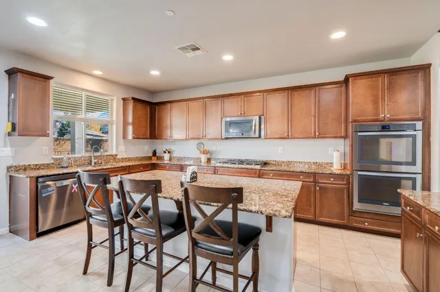 a kitchen with stainless steel appliances granite countertop a stove top oven a sink dishwasher a dining table and chairs with wooden cabinets